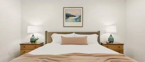 A neatly made bed with a striped pillow, two bedside tables with lamps, and a framed picture on the wall.