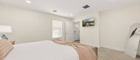 Une chambre à coucher comprenant un lit, une commode, un miroir et une porte donnant sur une autre pièce.