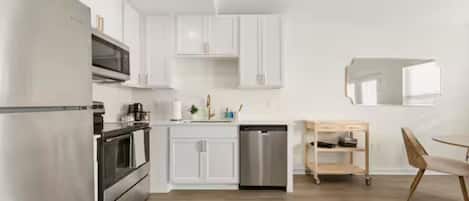 A modern kitchen with white cabinets, stainless steel appliances, and a wooden dining area.