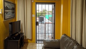 Una sala de estar con televisión, sofá, puerta corrediza de vidrio y un cuadro en la pared.