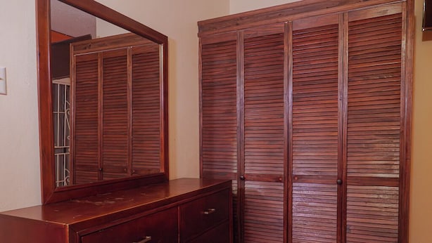 Un dormitorio con un aparador de madera, un espejo grande y un armario con puertas horizontales persianas.