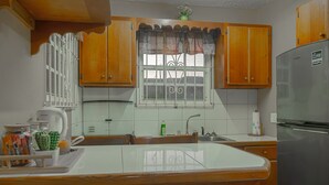 Una cocina con armarios de madera, un refrigerador de acero inoxidable, una ventana con cortina decorativa y un lavamanos.