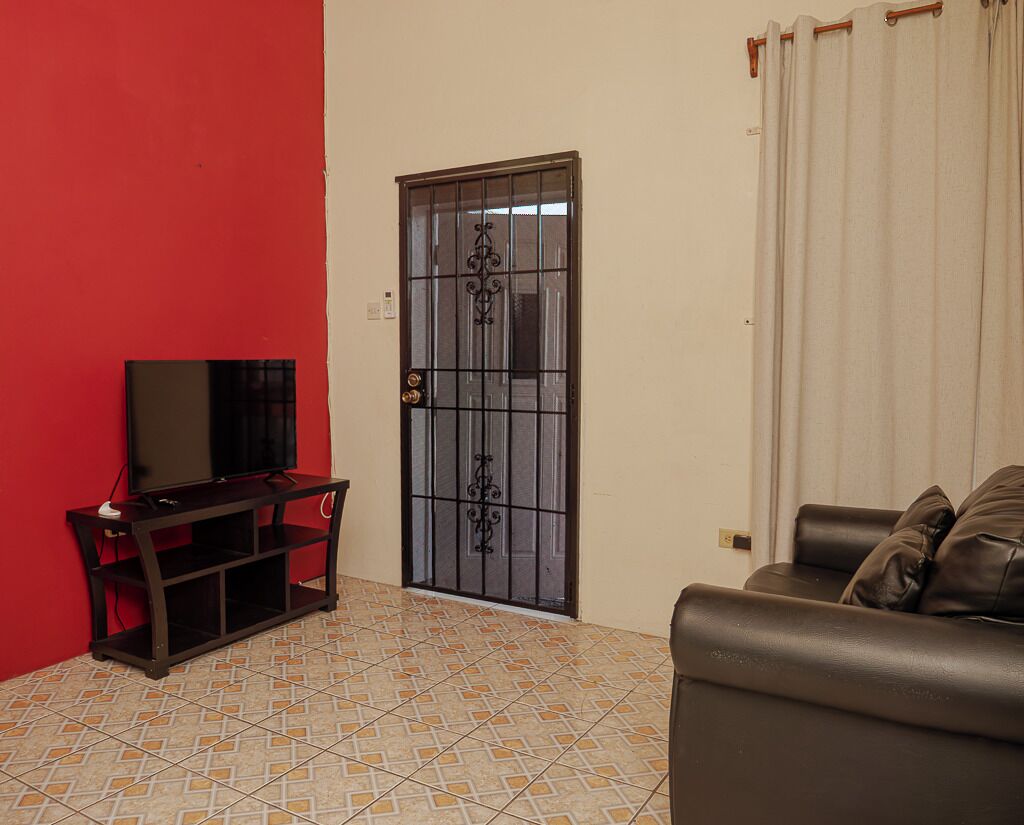 A living room with a television on a stand, a sofa, a door with a metal gate, and a tiled floor.