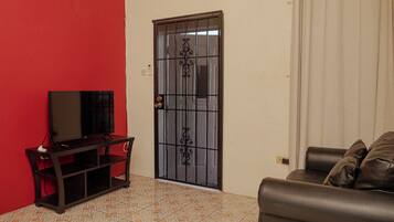 A living room with a television on a stand, a sofa, a door with a metal gate, and a tiled floor.