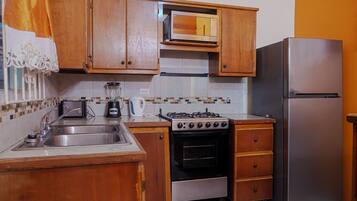 A kitchen with wooden cabinets, a stainless steel sink, a gas stove, an oven, and a refrigerator.