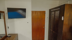 Una habitación con un armario de madera, un televisor montado en la pared y una puerta con detalles de madera.
