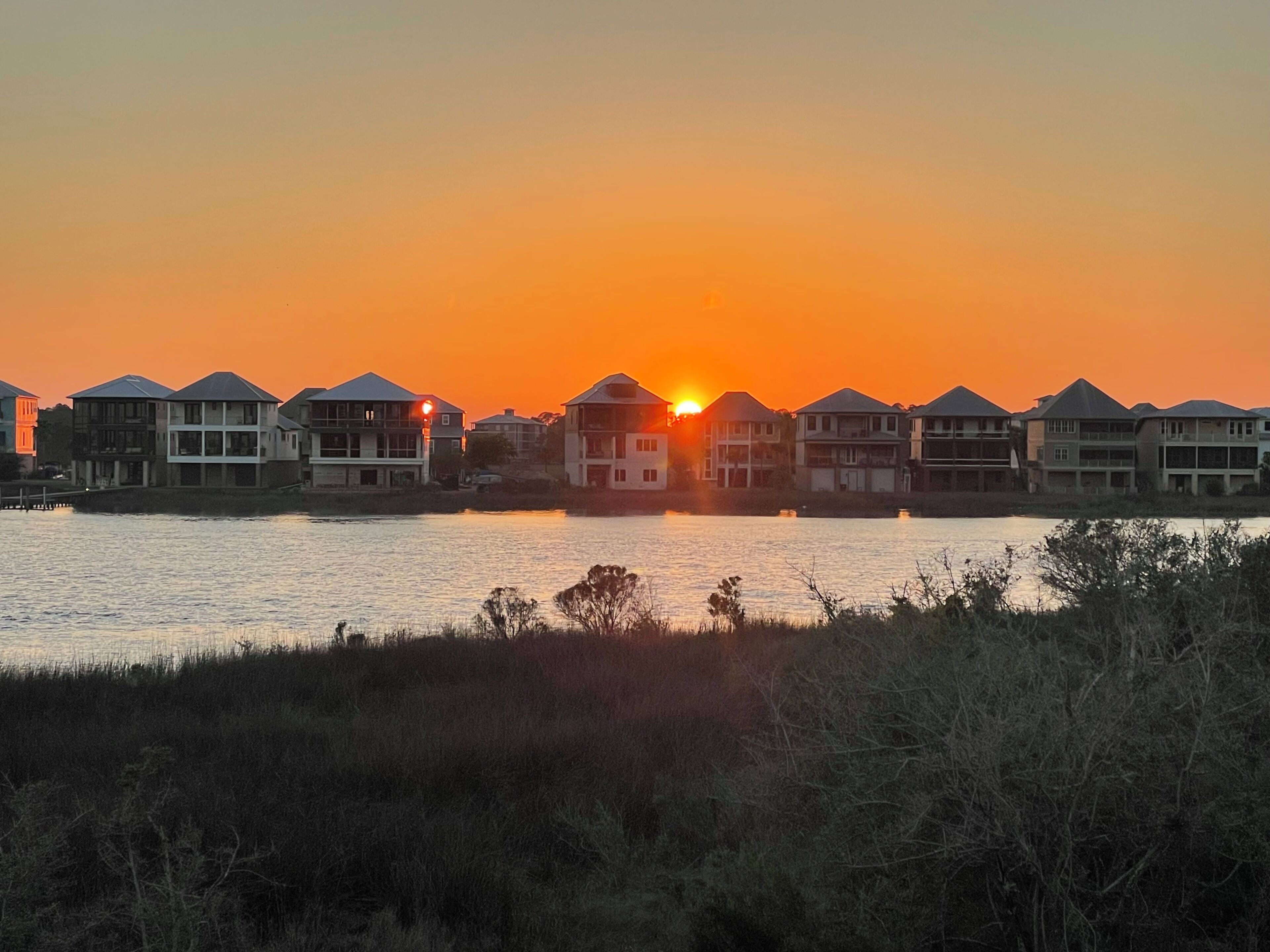 A waterfront property with multiple buildings, a sunset, and a calm body of water.