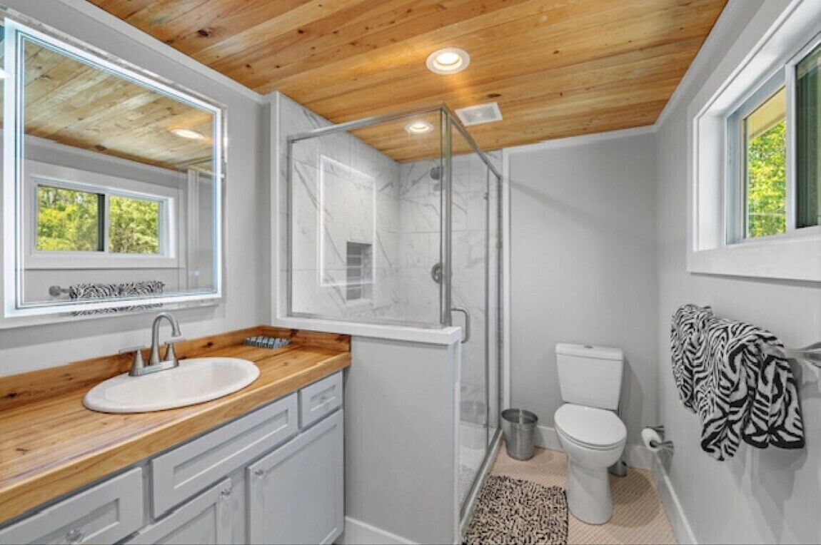 A bathroom with a wooden ceiling, a glass shower enclosure, a white sink, and a zebra-patterned towel.
