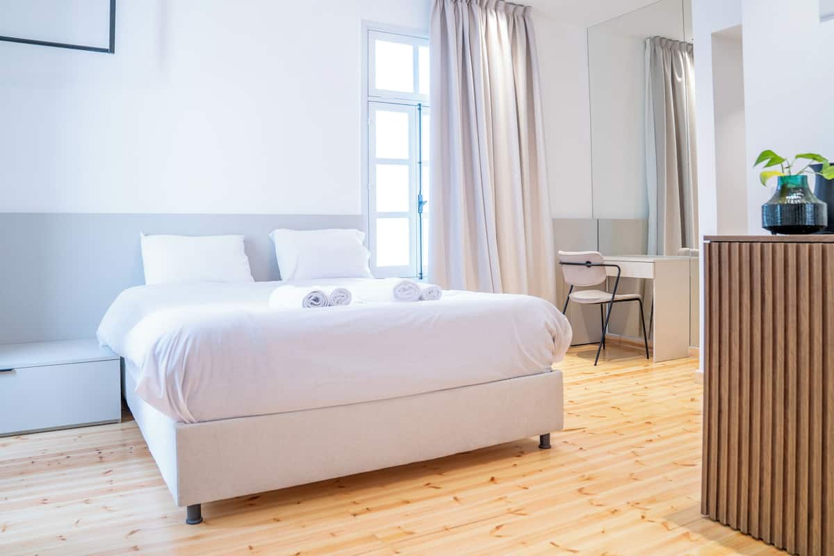 Ein modernes Hotelzimmer mit Bett, Schreibtisch, Stuhl und einer Topfpflanze.