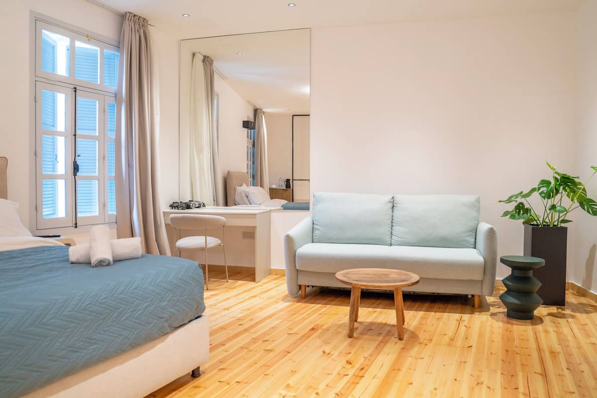 Ein Zimmer mit Bett, Schreibtisch, Sofa, kleinem Tisch und einer Zimmerpflanze.