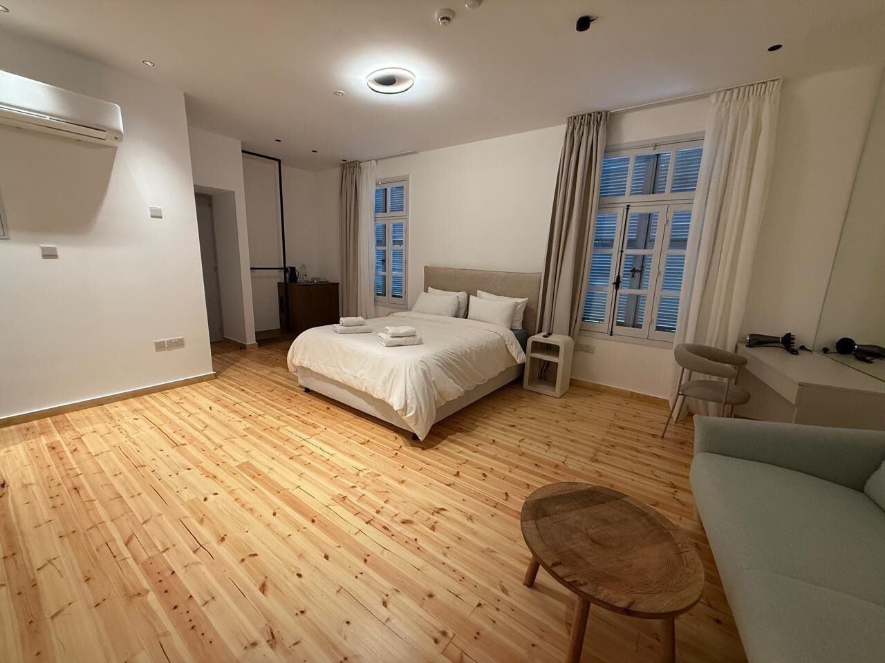 A bedroom with a bed, a wooden floor, a sofa, a chair, and a window with curtains.