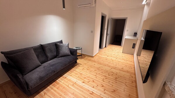 Un salon moderne avec un canapé gris foncé, une petite table d’appoint et un plancher en bois.