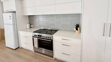 Una cucina moderna con mobili bianchi, un fornello a gas, un forno e un frigorifero.