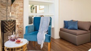 Een woonkamer met een blauwe stoel, een bruine bank, een klein rond tafeltje met een theepot, en een boekenkast op de achtergrond.
