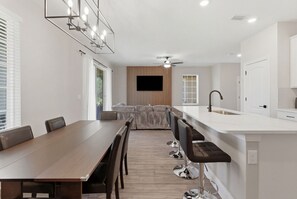 A modern kitchen with a central island, a dining area with a long table and chairs, and a built-in TV. - Modern Single-Family w/ Game Room | Reunion Village (7748) (Kissimmee)