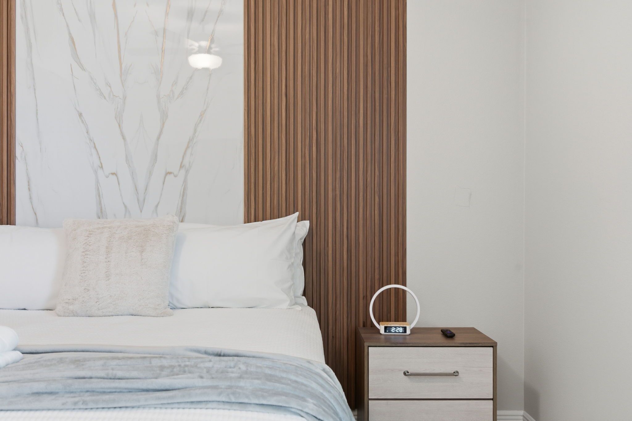 Un dormitorio con una cama, una mesita de noche y una pared con listones de madera verticales.