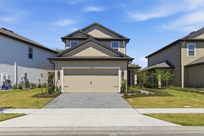 A modern two-story house with a beige garage door, a paved driveway, and a well-maintained lawn. - Modern Single-Family w/ Game Room | Reunion Village (7748) (Kissimmee)