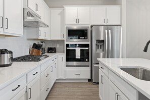 A modern kitchen with white cabinetry, stainless steel appliances, and a built-in oven. - Modern Single-Family w/ Game Room | Reunion Village (7748) (Kissimmee)