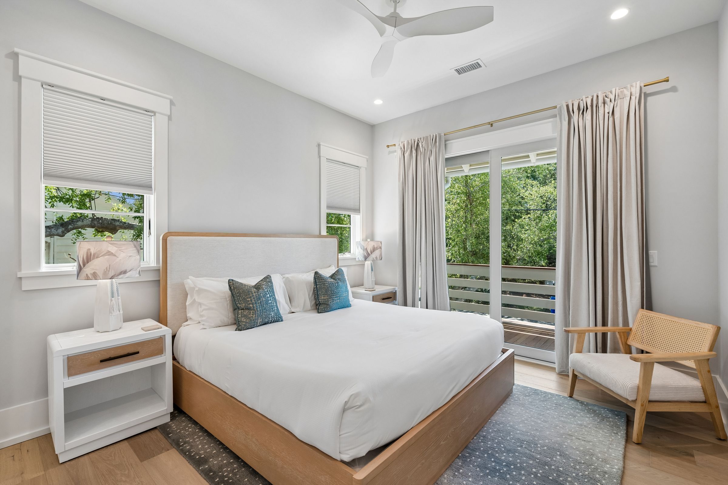 A bedroom with a bed, nightstands, a chair, and a view of greenery.