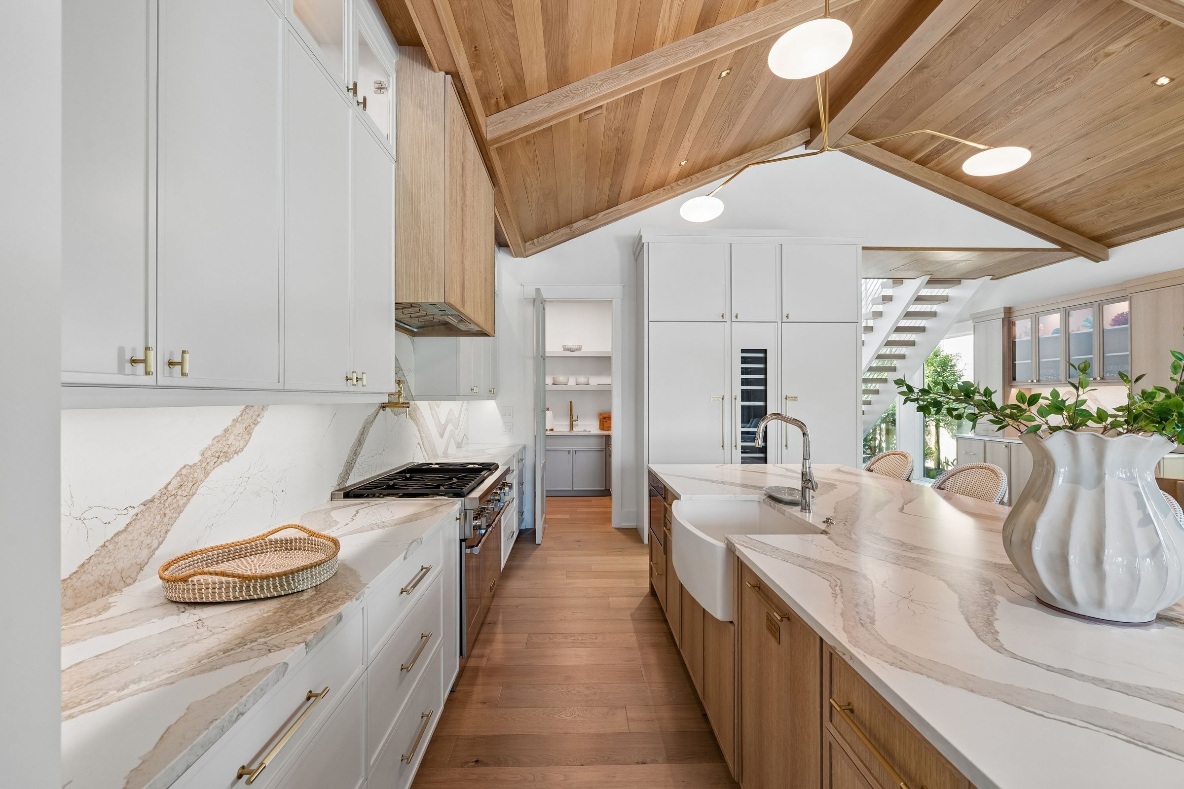 A modern kitchen with white cabinetry, a wooden ceiling, and a marble countertop.