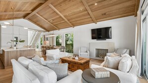 Ein geräumiger Wohnbereich mit hoher Decke, einem Holzes Esstisch, weißen Sofas und einem Kamin.