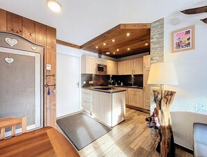 A kitchen with wooden cabinets, a central island, and a hanging lamp. - 200m from resort center, 3rd floor, swimming pool, balcony, tv, ski locker, 40m², Le Corbier (Le Corbier)