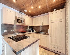 A modern kitchen with wooden cabinets, a built-in microwave, a stove, and a sink. - 200m from resort center, 3rd floor, swimming pool, balcony, tv, ski locker, 40m², Le Corbier (Le Corbier)