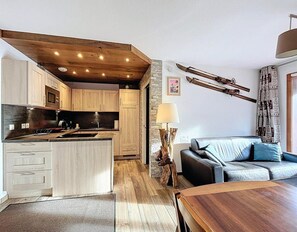 A modern kitchen with wooden cabinets, a central island, and a dining area with a wooden table. - 200m from resort center, 3rd floor, swimming pool, balcony, tv, ski locker, 40m², Le Corbier (Le Corbier)