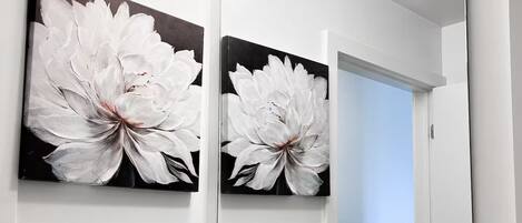 A bathroom with a white sink, a mirror, and a painting of white flowers.