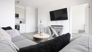 A modern living room with a sofa, a coffee table, a TV, and a kitchen area in the background. - Skyline Presidential Condo | Bowling Alley,Gym,Pool,Hot Tub,Sauna,Lounge (Kitchener)