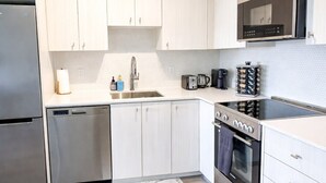 A modern kitchen with white cabinets, stainless steel appliances, a microwave, and a dishwasher. - Skyline Presidential Condo | Bowling Alley,Gym,Pool,Hot Tub,Sauna,Lounge (Kitchener)