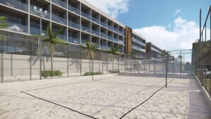 Un hotel de varios pisos con balcones, una cancha de tenis cercada y palmeras.