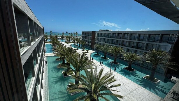 Un hotel con piscina, palmeras y vista al océano.