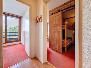 A room with a red carpet, wooden flooring, a sliding door, and a view of greenery outside. - At the foot of shops, 2nd floor, balcony, tv, ski locker, 30m², Les Menuires (Les Menuires)