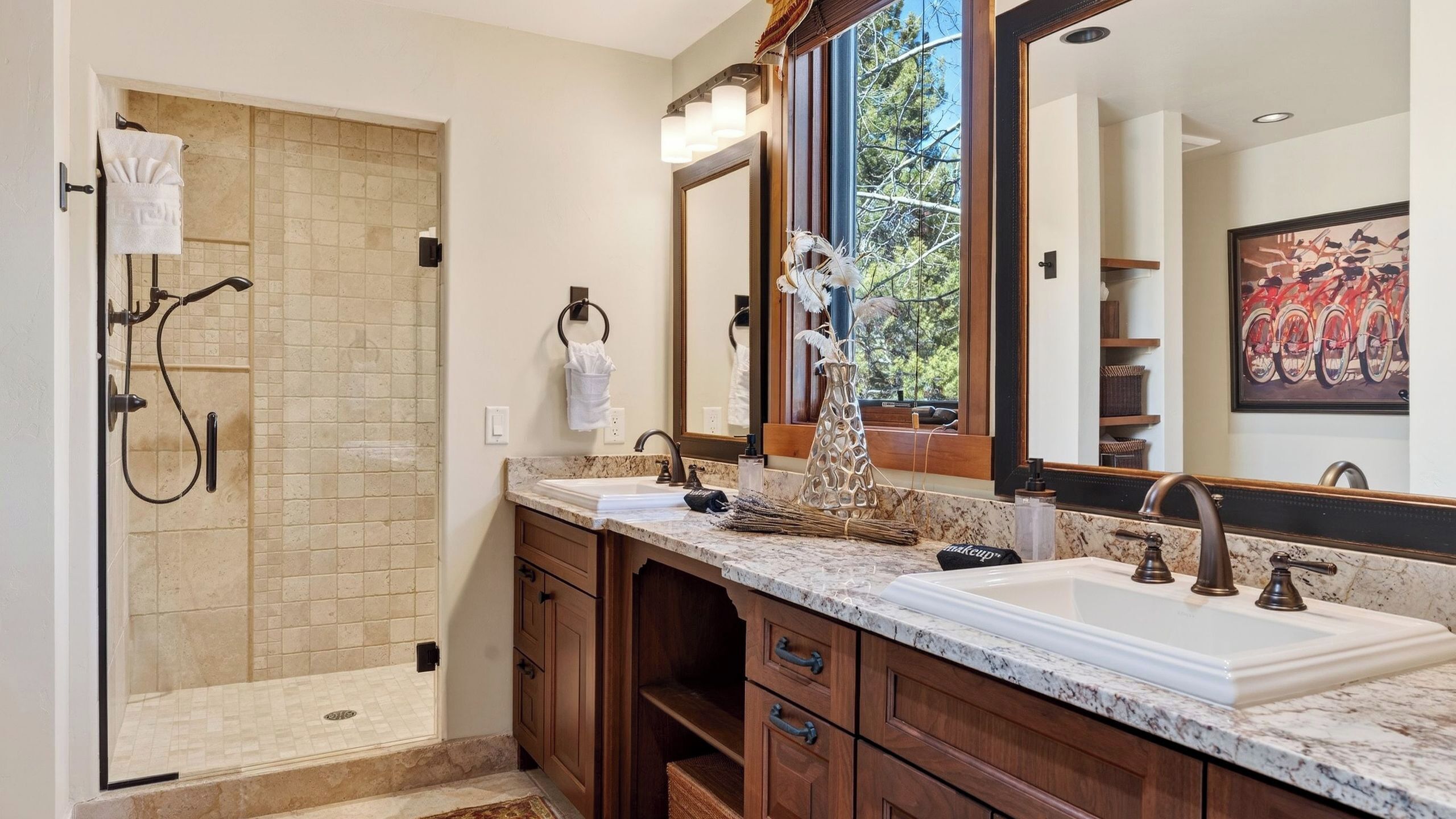 A bathroom with a walk-in shower, two sinks, a large mirror, and a window with a view.