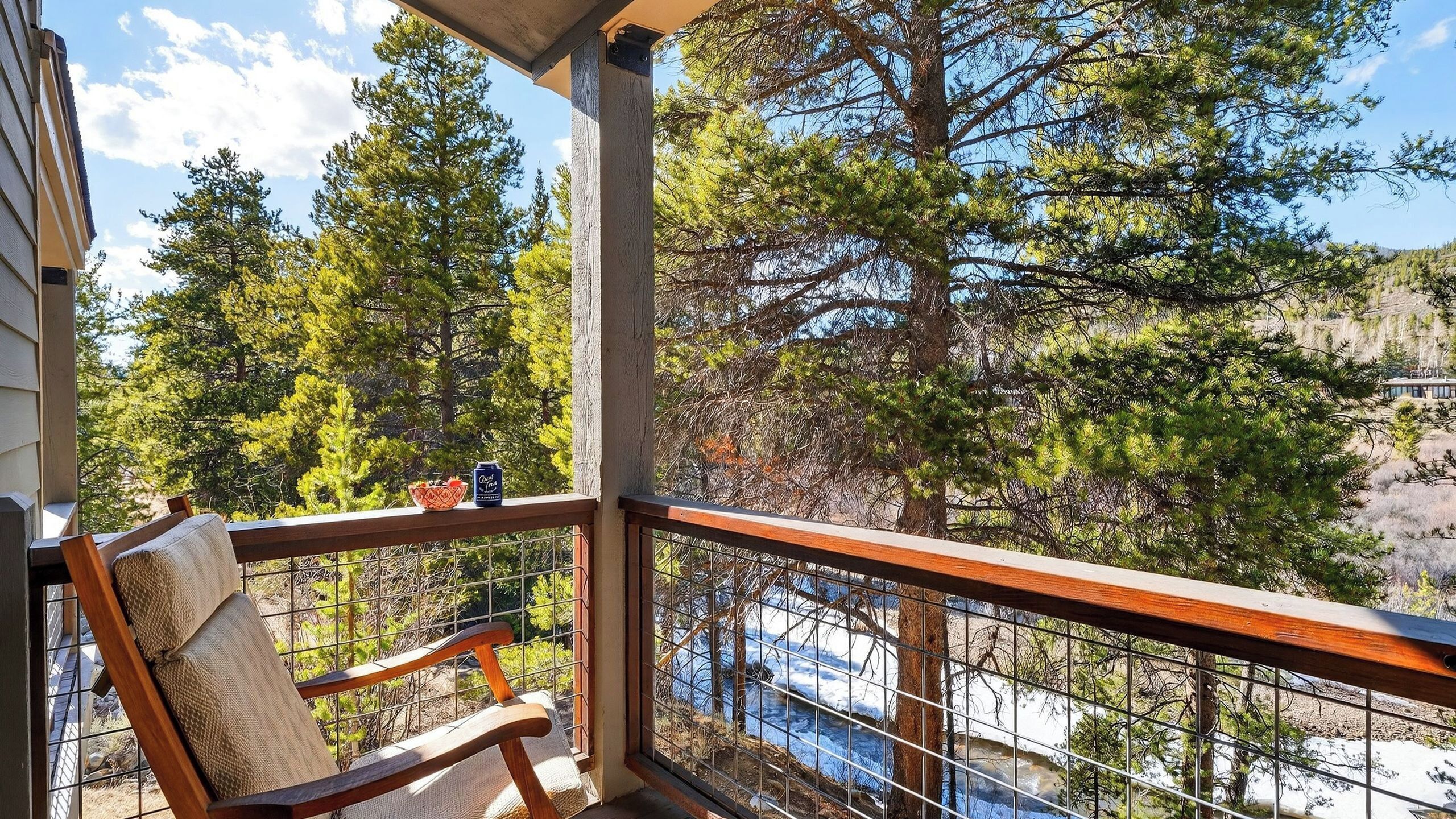 A balcony with a wooden chair, a metal railing, and a view of trees and a river.