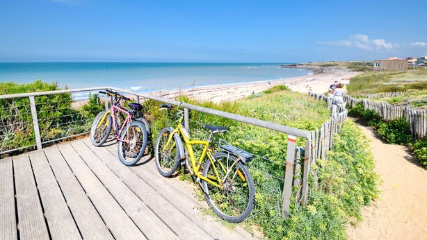 Ein Holzsteg führt zu einem Strand, entlang des Geländers sind Fahrräder abgestellt.