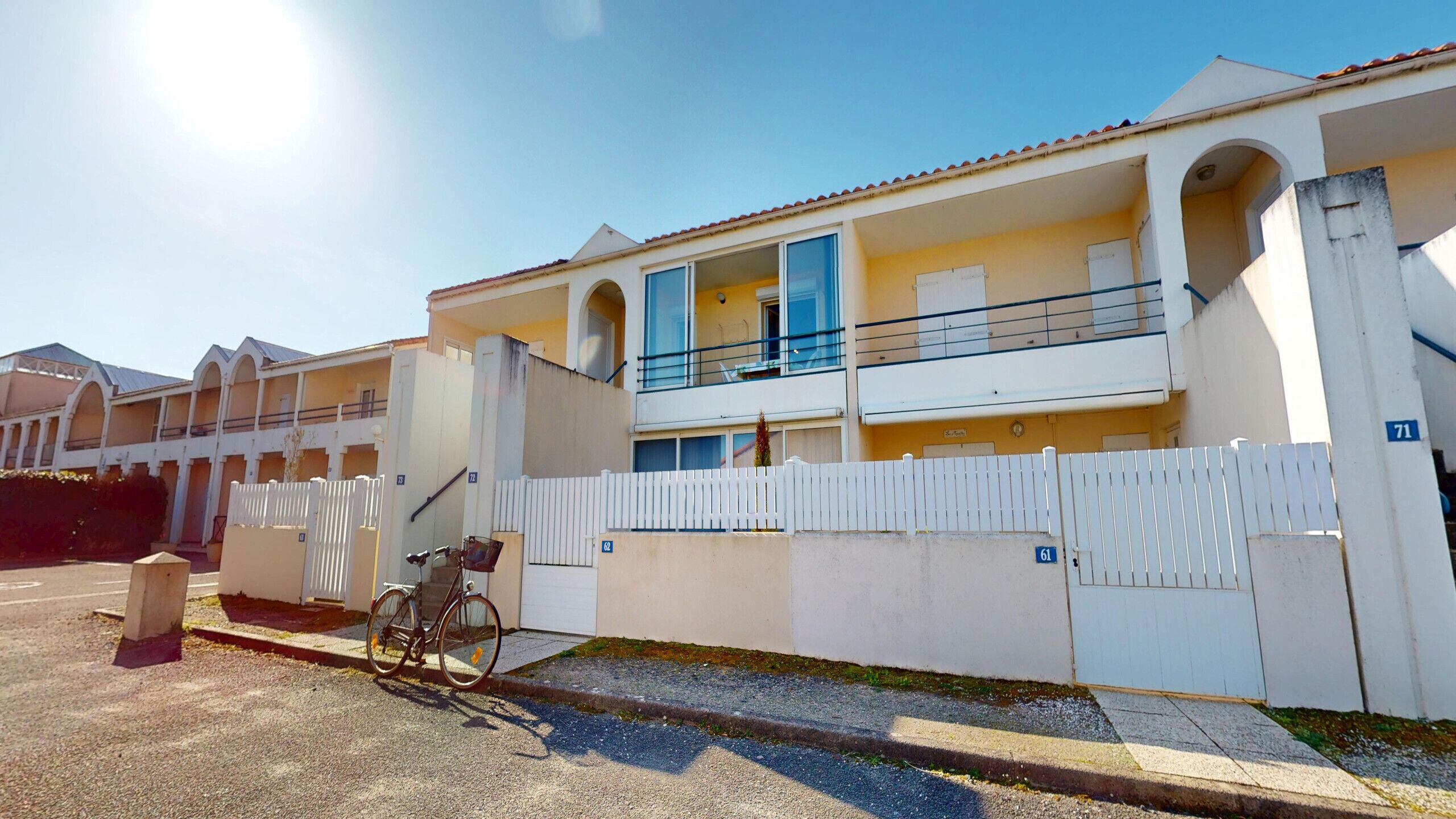 Un edificio de varios pisos con balcones, una cerca blanca y una bicicleta estacionada adelante.
