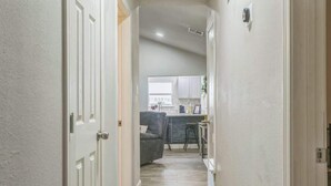 A narrow hallway leading to a kitchen area with a grey sofa and a window. - Cozy 3BR House in Prime Location (San Antonio)