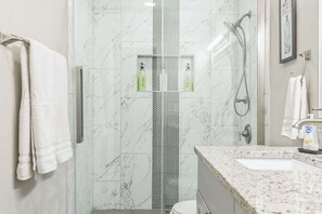 Ein modernes Badezimmer mit Dusche, Waschbecken und zwei Shampooflaschen auf der Ablagefläche.