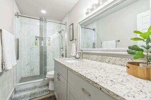A bathroom with a glass shower enclosure, a sink with a marble countertop, and a large mirror.