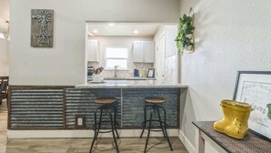 A kitchen with a central island, two stools, and a yellow decorative item. - Cozy 3BR House in Prime Location (San Antonio)