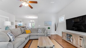A living room with a sectional sofa, a coffee table, a TV, and a ceiling fan. - Driftwood Dunes (Pensacola)