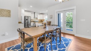 A modern kitchen with white cabinets, stainless steel appliances, and a dining area with a wooden table and chairs. - Driftwood Dunes (Pensacola)