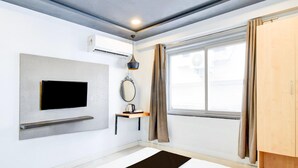 A modern hotel room with a flat-screen TV, a small table, a mirror, and a window with curtains. - Deluxe With Twin Bed Super Townhouse (Hyderabad)