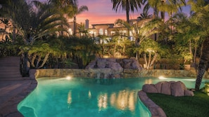A swimming pool surrounded by palm trees and a stone wall with a waterfall feature.