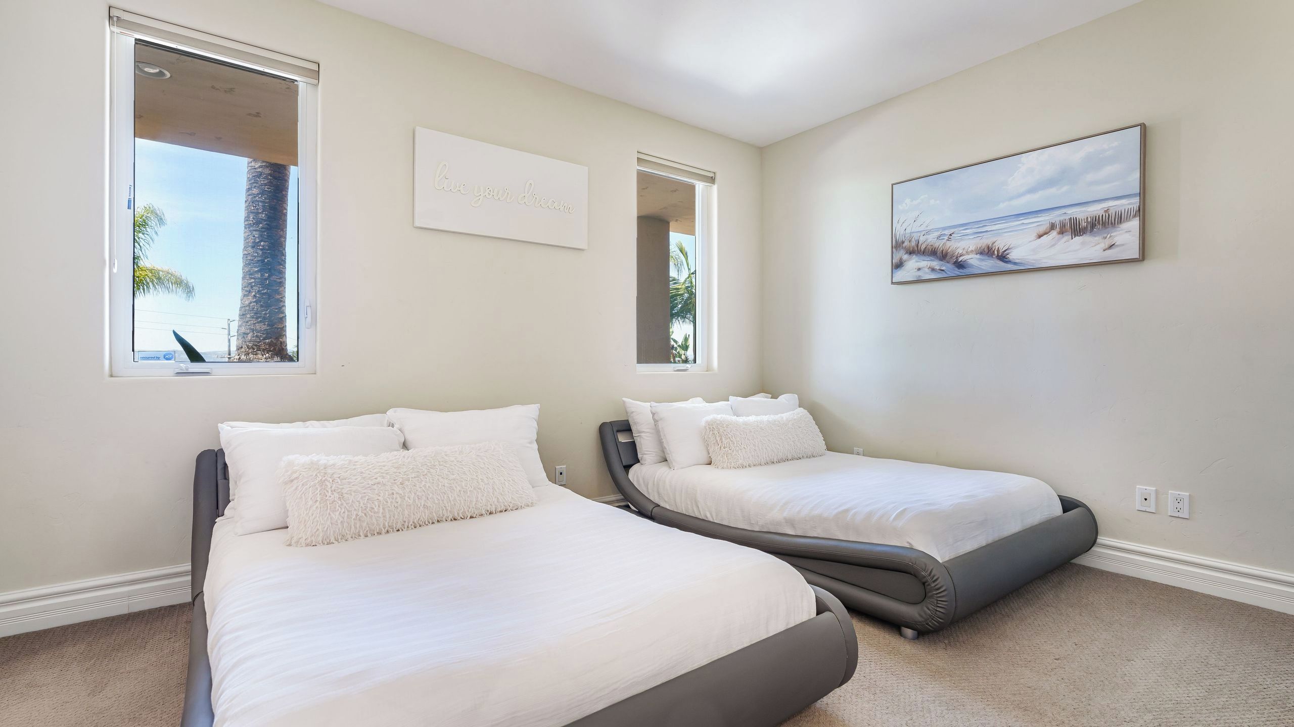A bedroom with two beds, a painting, and a sign that says 'live your dream.'