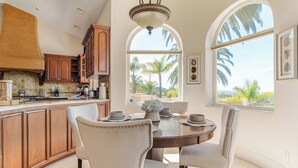 A kitchen with wooden cabinets, a dining table with chairs, and large windows with a view of palm trees. - Sunset Estate by Avantstay Sleeps 20 Resort-style Pool + Gorgeous Grounds Exclusive Poway Stay (Poway)