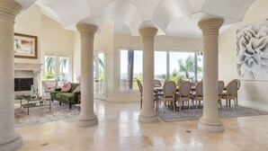 A spacious living area with a fireplace, a green sofa, a dining table with chairs, and large windows with a view. - Sunset Estate by Avantstay Sleeps 20 Resort-style Pool + Gorgeous Grounds Exclusive Poway Stay (Poway)