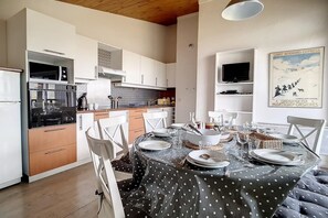 A modern kitchen with white cabinets, a dining table set for four, and a television on a shelf. - Ski-in/ski-out & foot of the slopes, 3rd floor, view mountain, balcony, tv, ski locker, 66m² (Les Menuires)